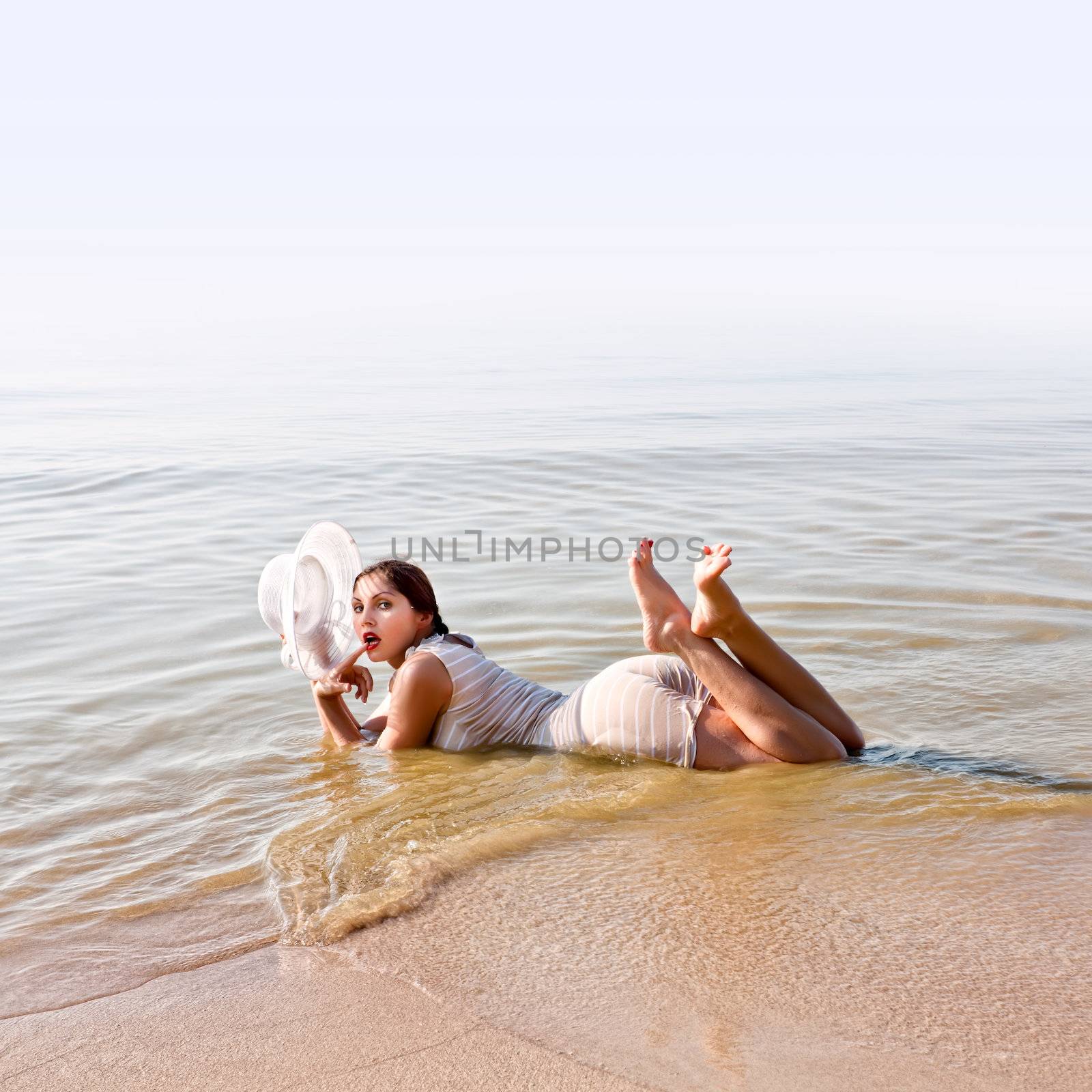 Woman in white hat  lies in the water at the beach by palinchak