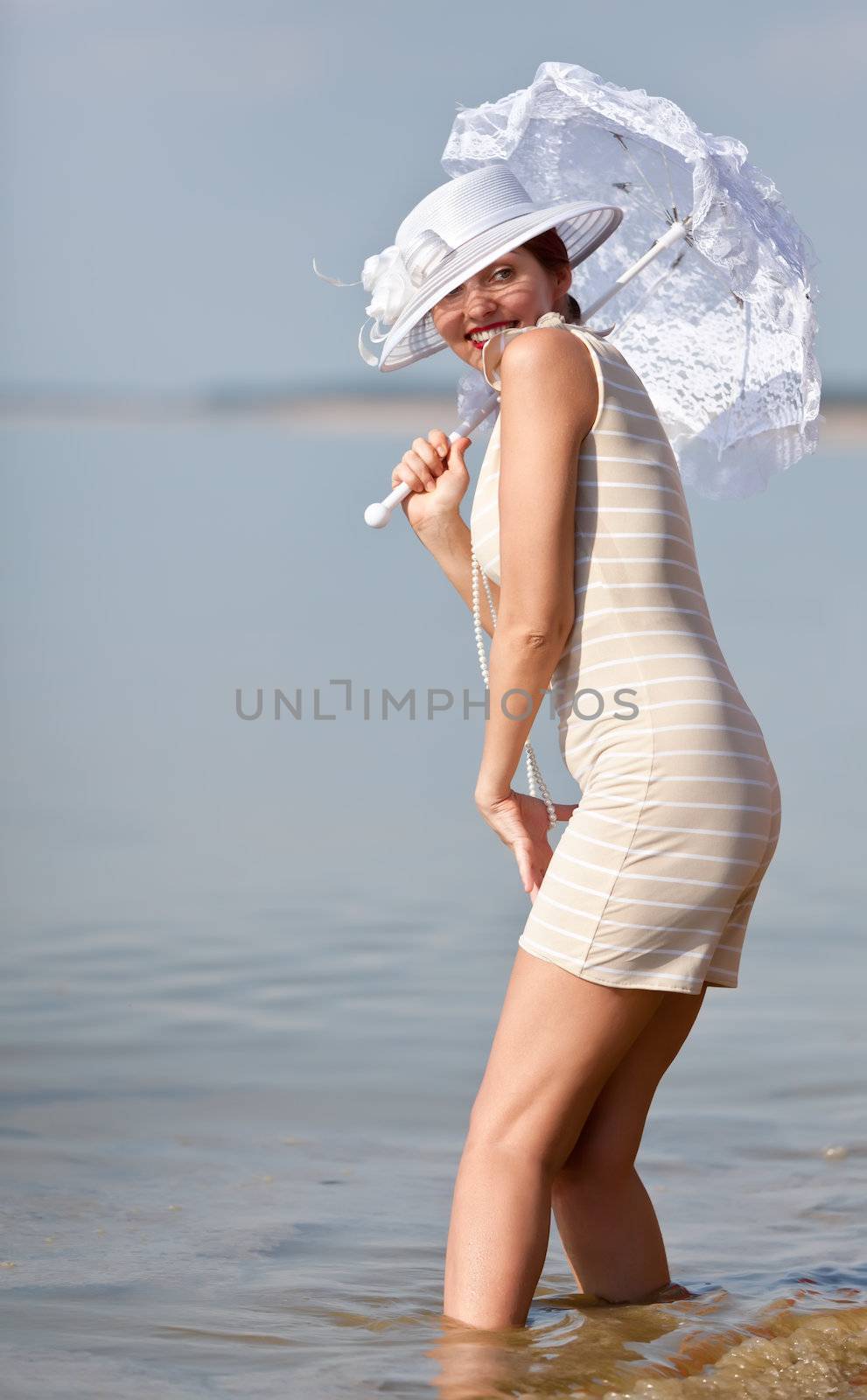 Woman in a striped retro bathing suit with a white parasol against the sea