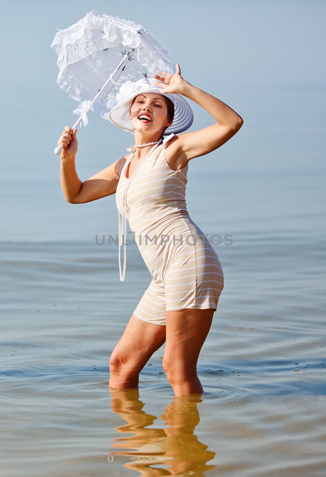 Woman in a striped retro bathing suit with a white parasol against the sea