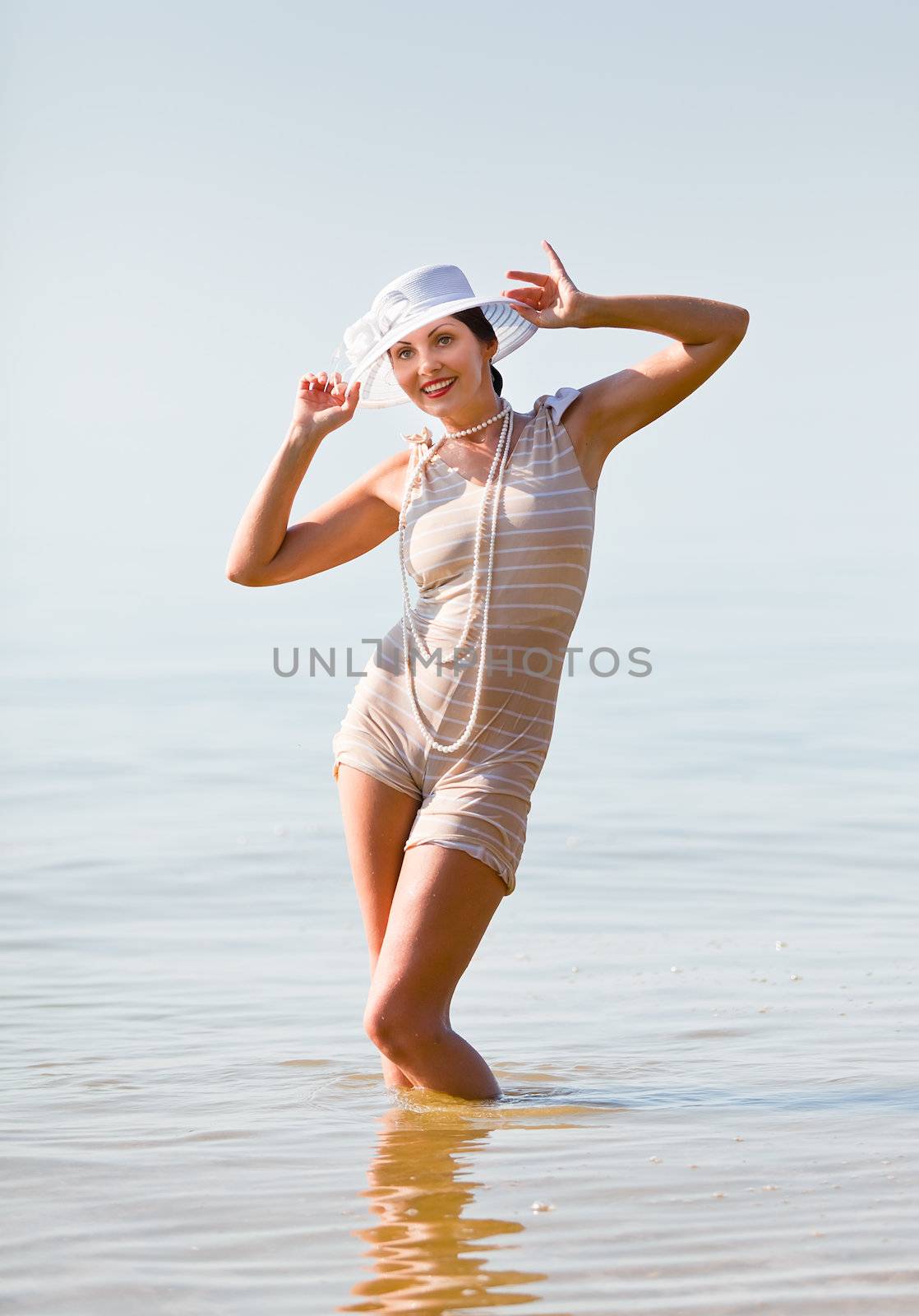 Woman in a striped retro bathing suit in the white hat posing against the sea