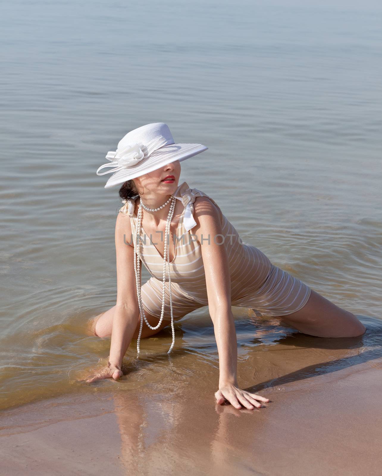Woman in a striped retro bathing suit in the white hat posing against the sea