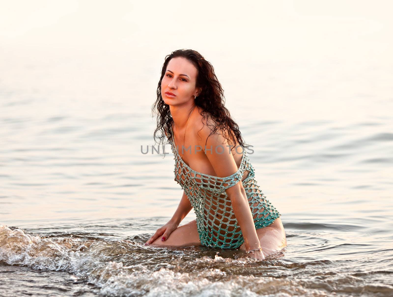 Seminude girl sitting on the beach in the waves in the evening light