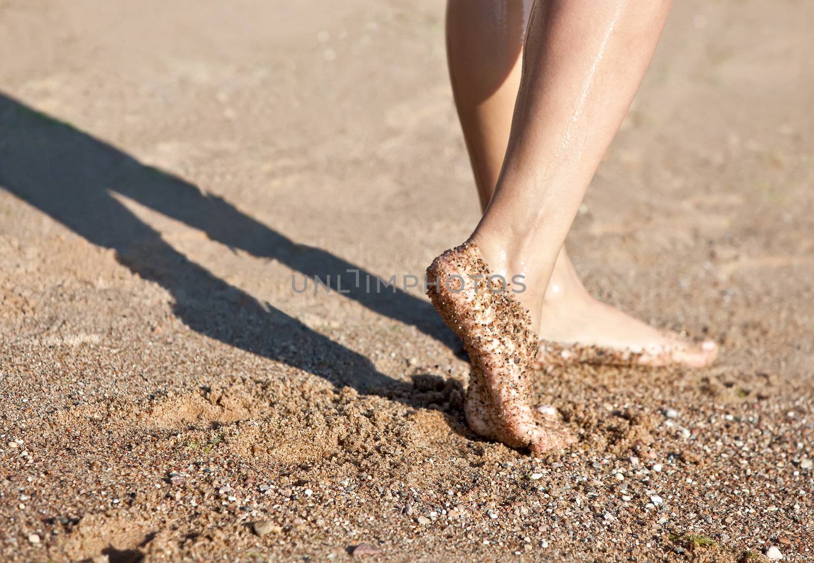 Girl's barefoot legs on the sand beach