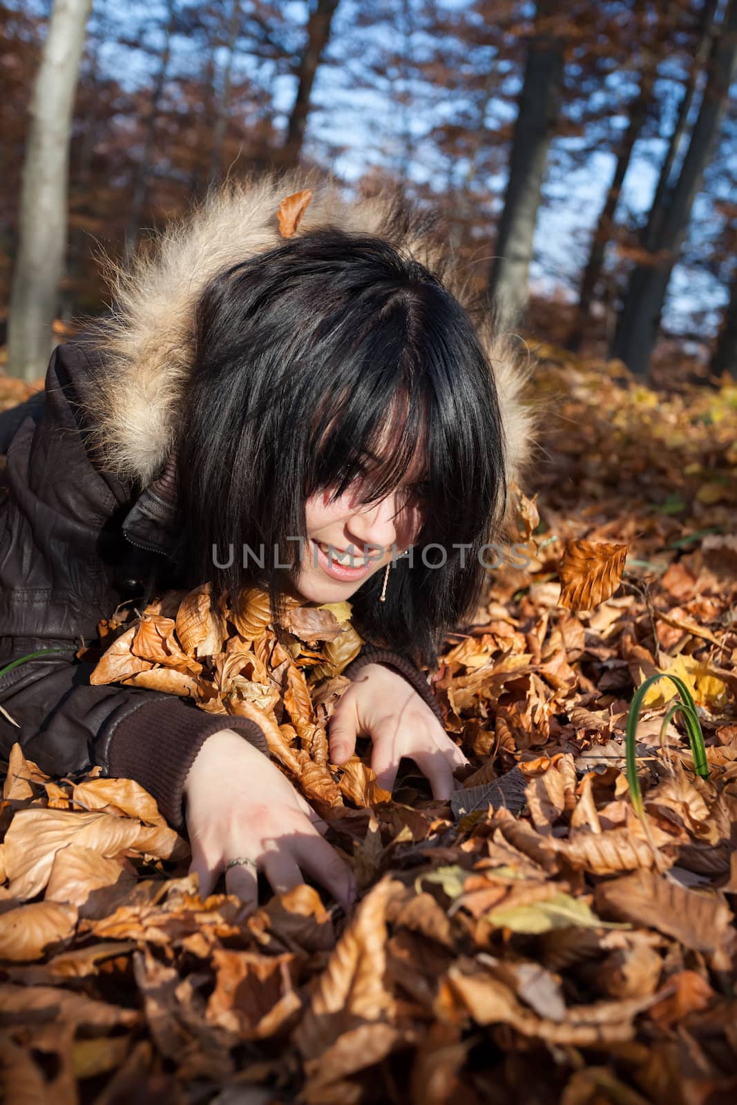 Girl playing with fallen autumn leaves in the forest
