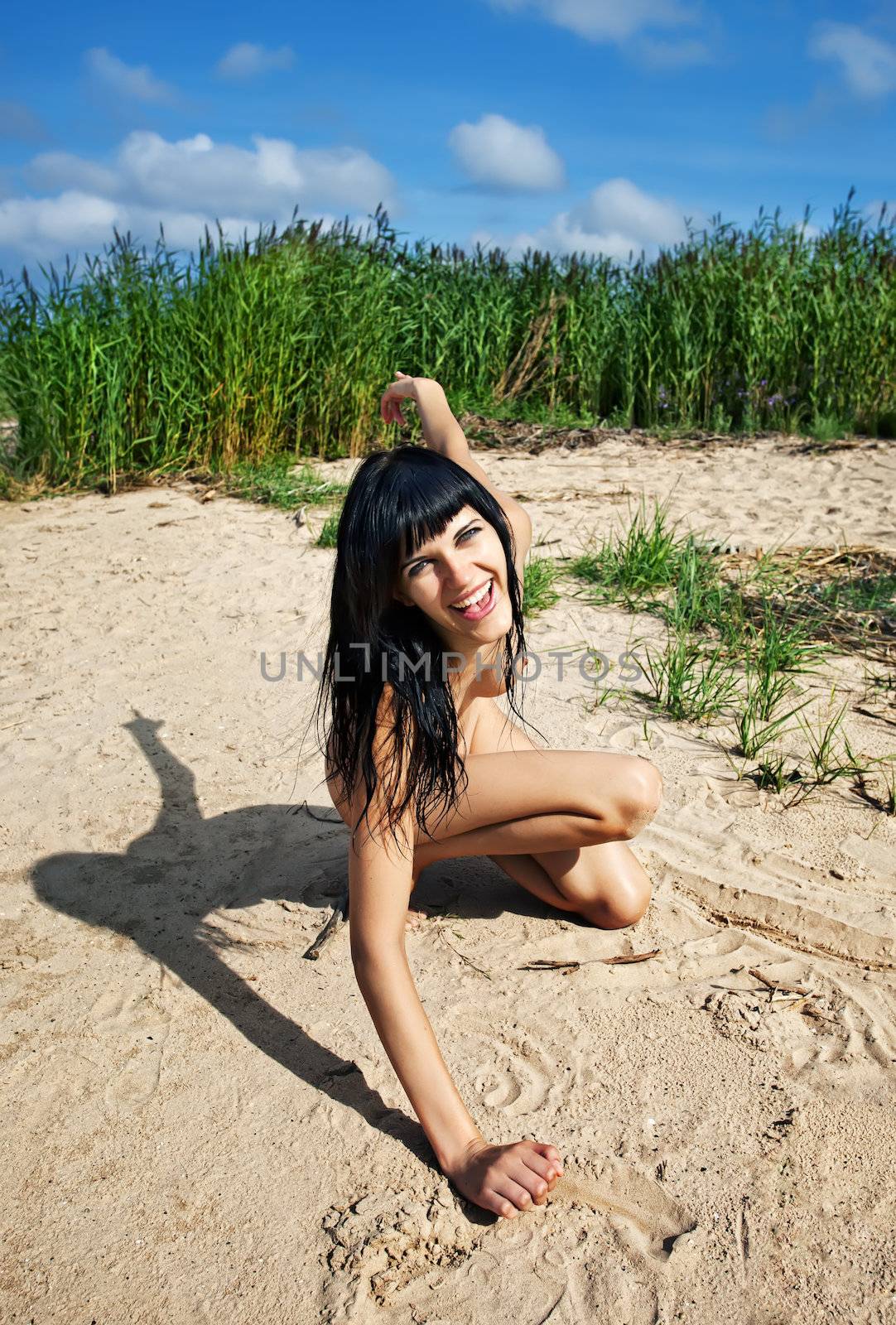 Young nude girl smiling and playing in the sand