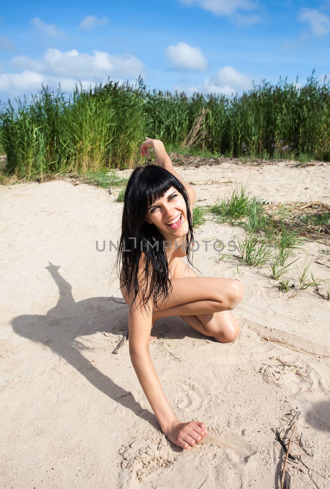 Young nude girl smiling and playing in the sand