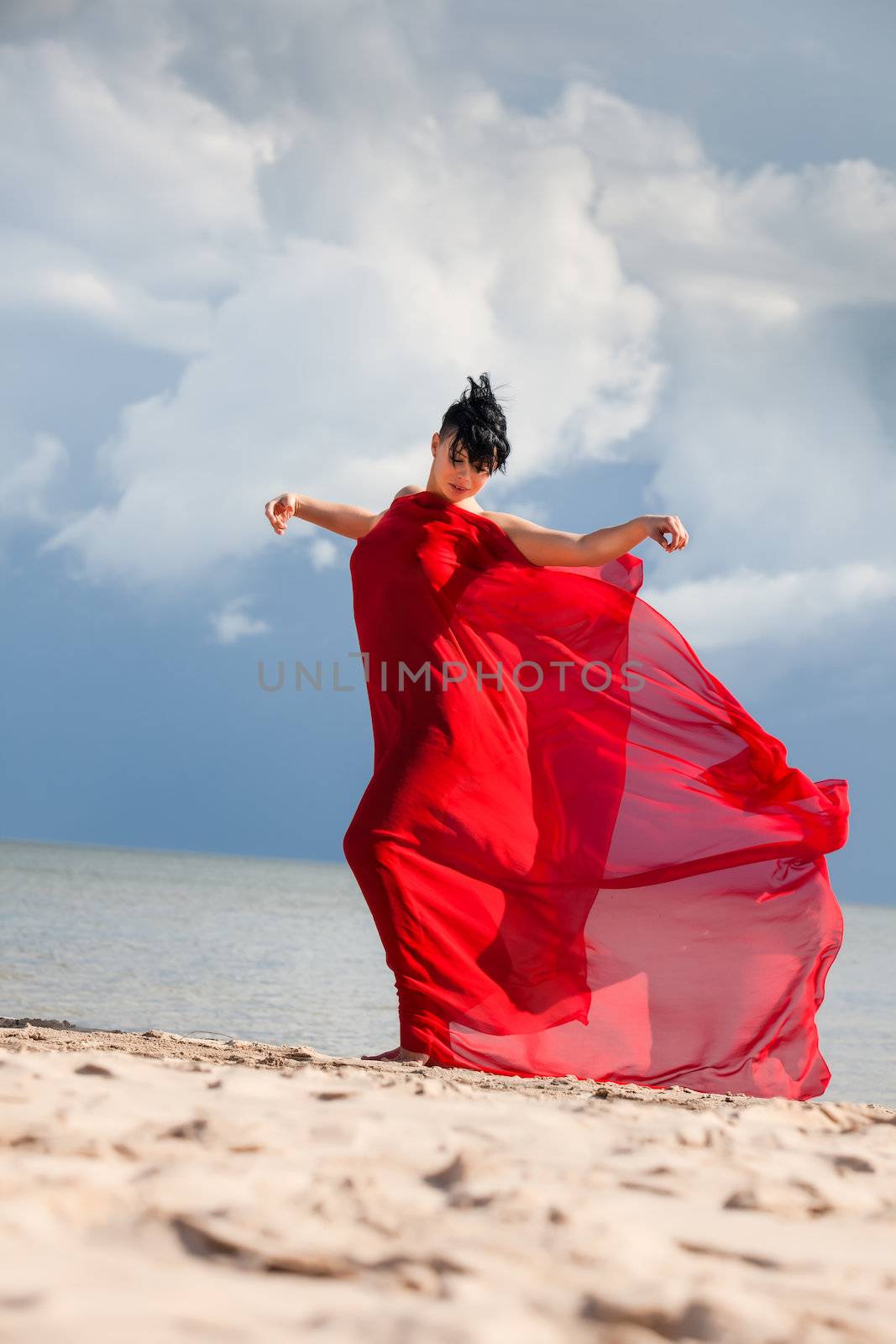 Young naked woman on a beach with red fabric