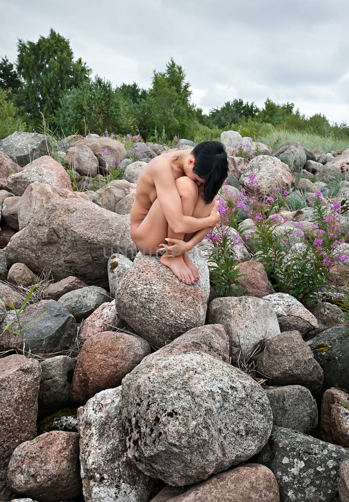 Beautiful nude woman sitting on stones against nature background