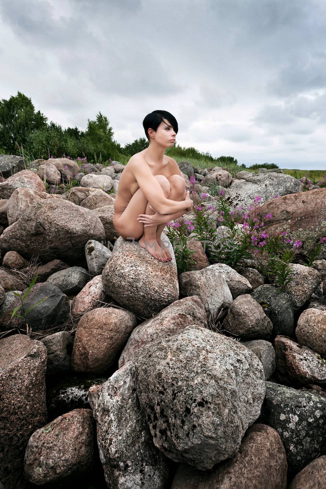 Beautiful nude woman sitting on stones against nature background