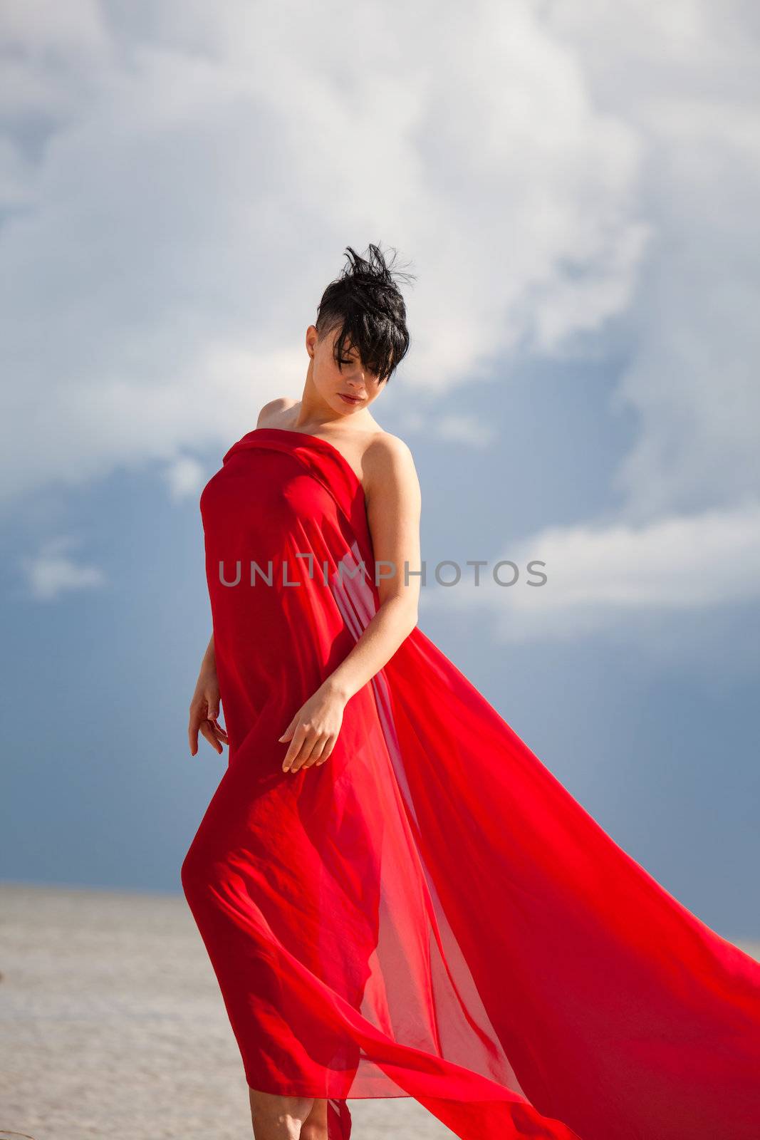 Young naked woman on a beach with red fabric
