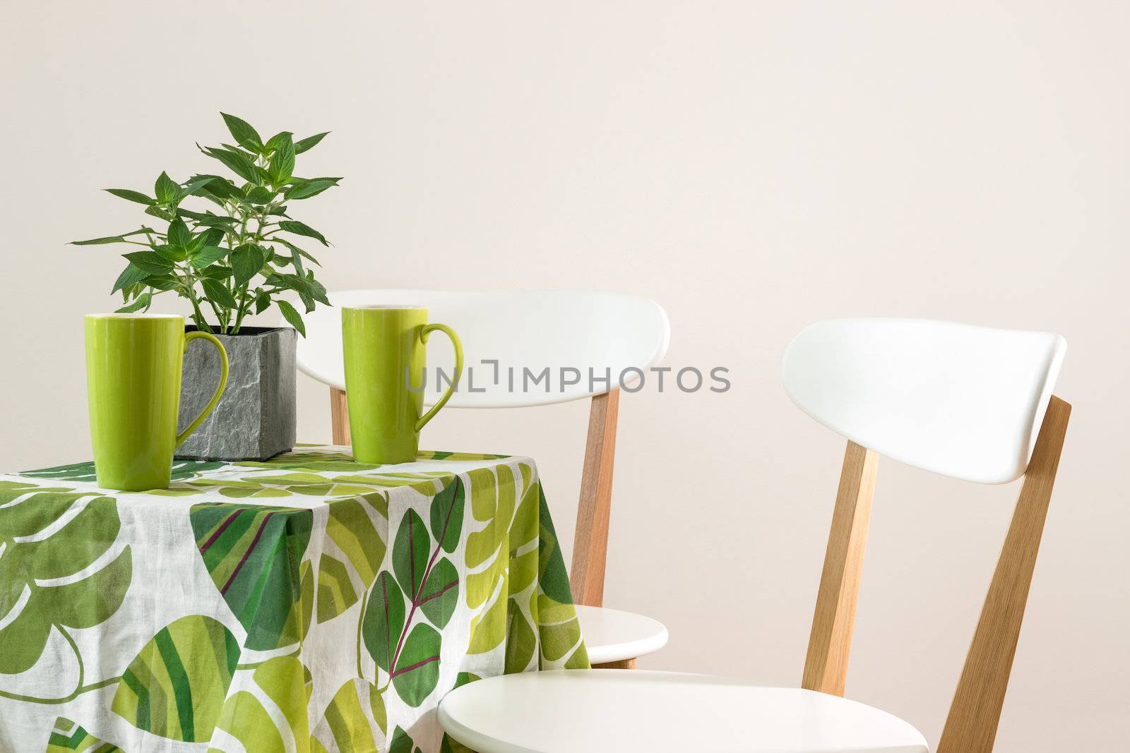 Two chairs and bright table with teacups and mint in a pot.