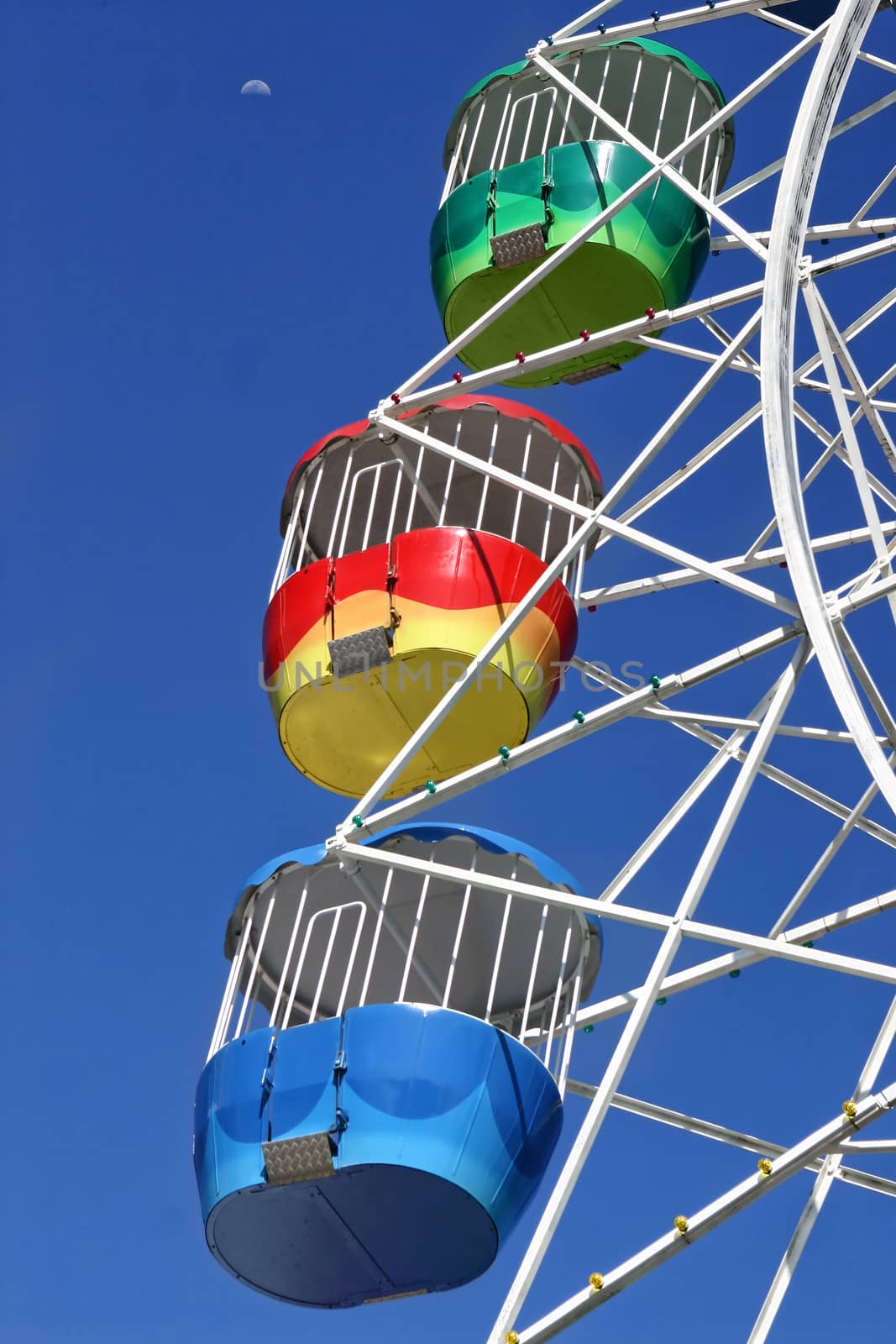 Closeup of Ferris Wheel gondolas against deep blue sky with moon.