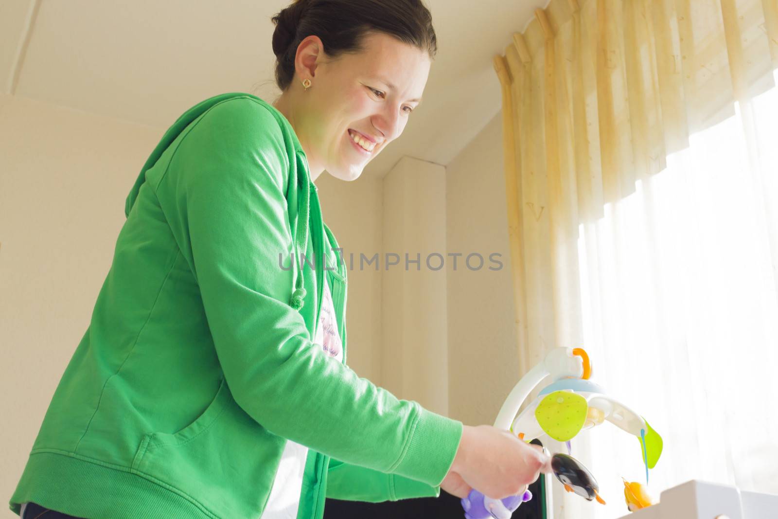 mother runs a music windup toy over the baby's crib by Tetyana
