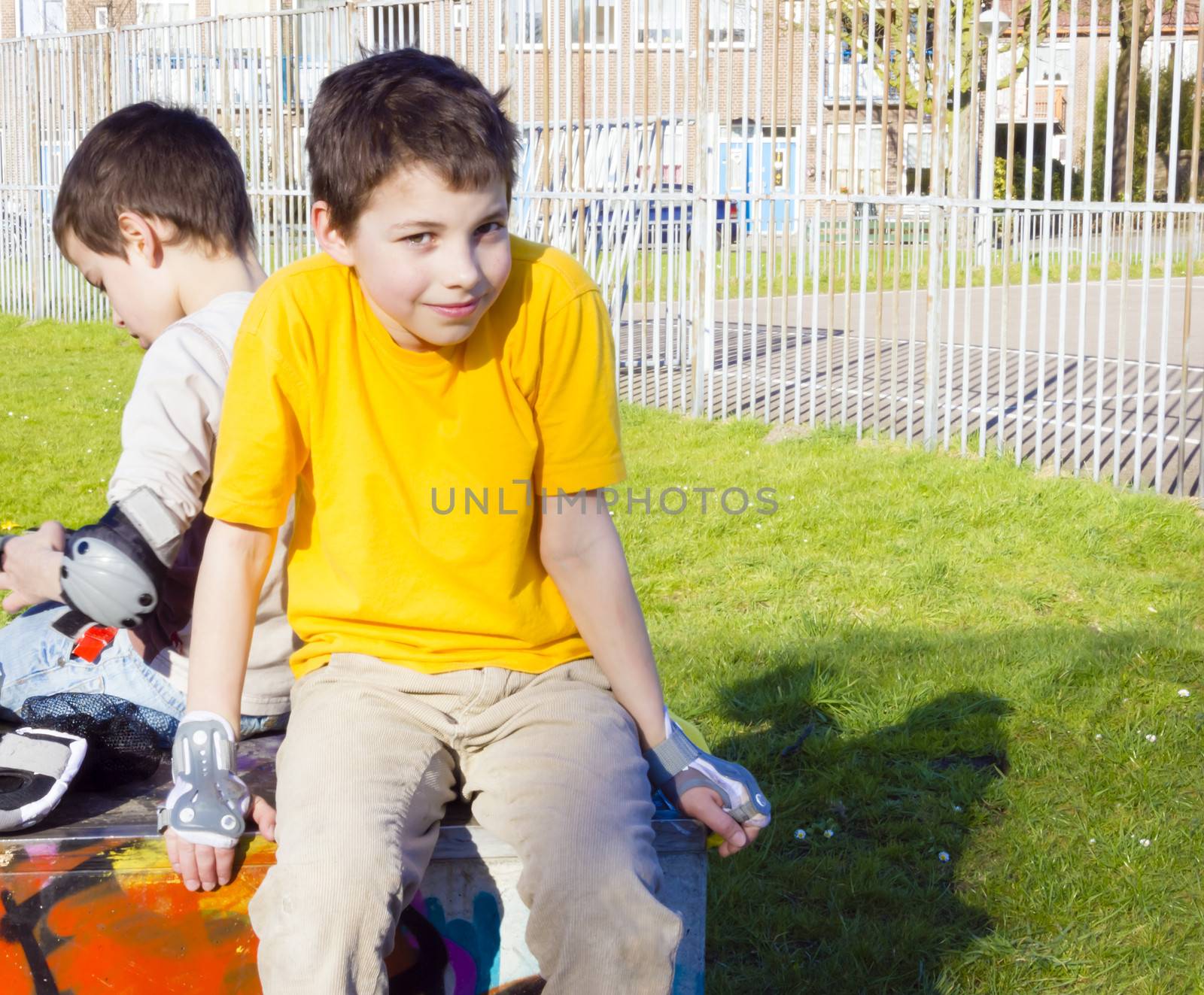 two cute boys in roller-blading protection kits sitting in playground