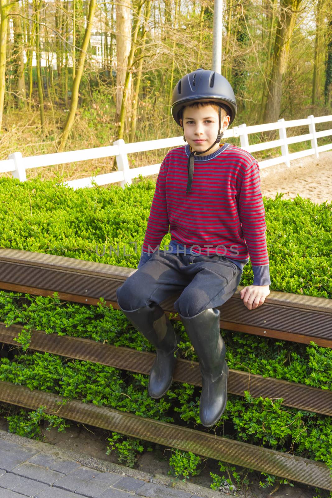 cute teenage  boy in helmet and boots for horse riding sitting n by Tetyana