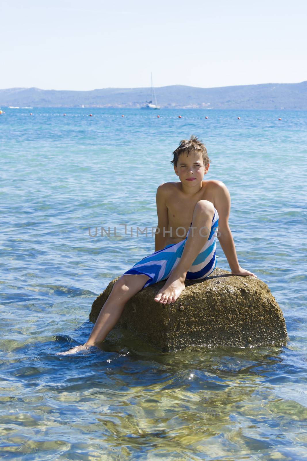 Cute eleven years old boy sitting on a rock in the sea