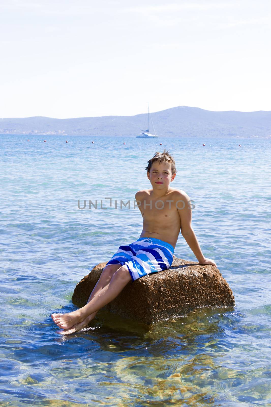 Cute eleven years old boy sitting on a rock in the sea