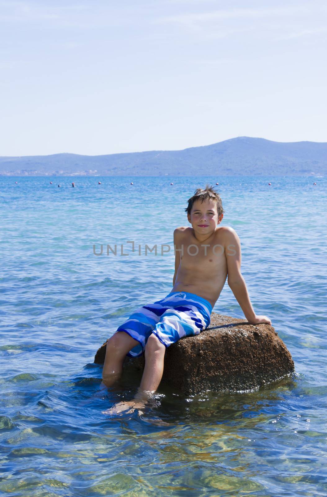 Cute eleven years old boy sitting on a rock in the sea