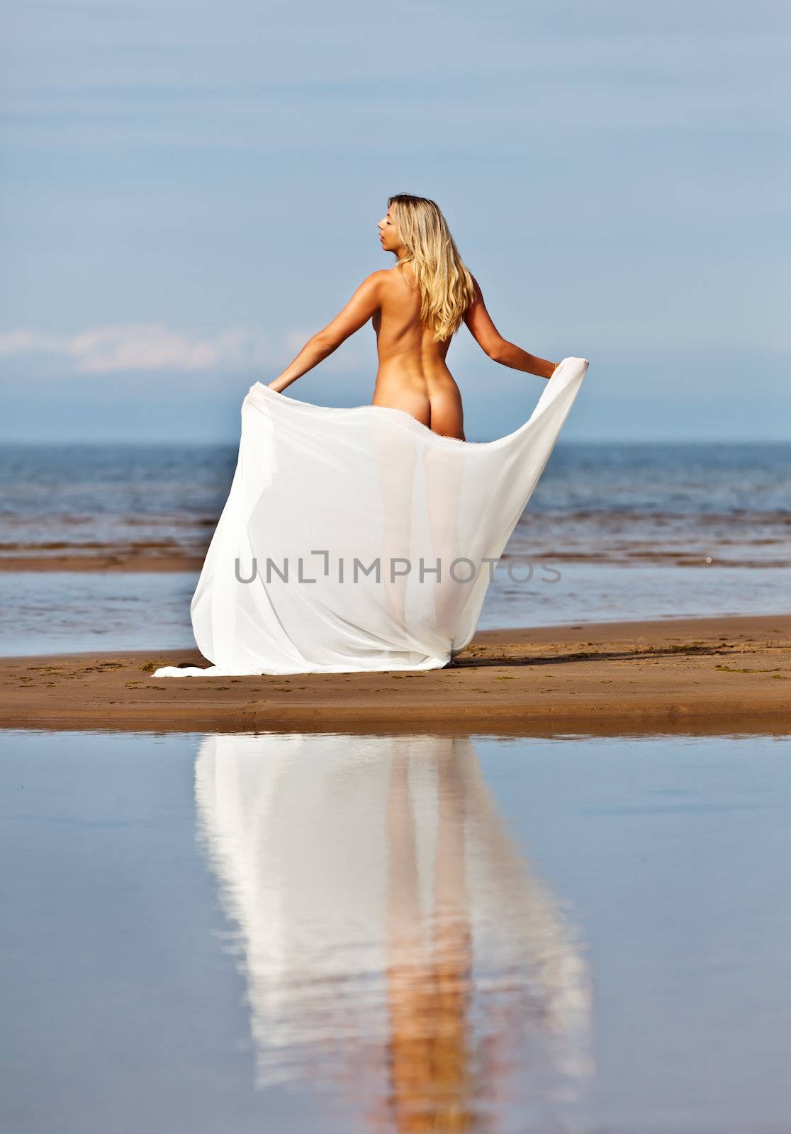 Naked woman on the beach with a white cloth and water reflection
