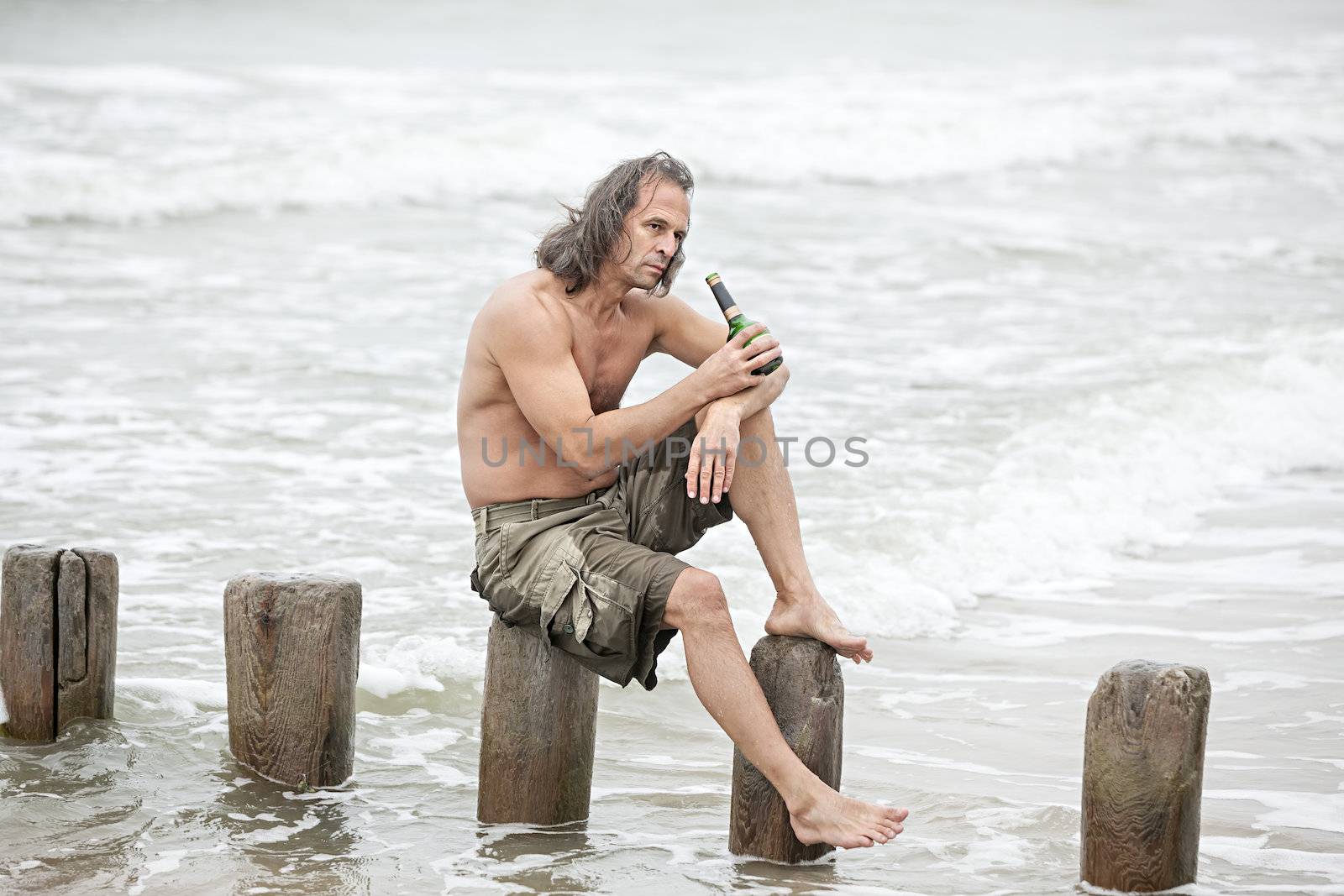 Middle-aged man sitting near the sea and drinking alcohol