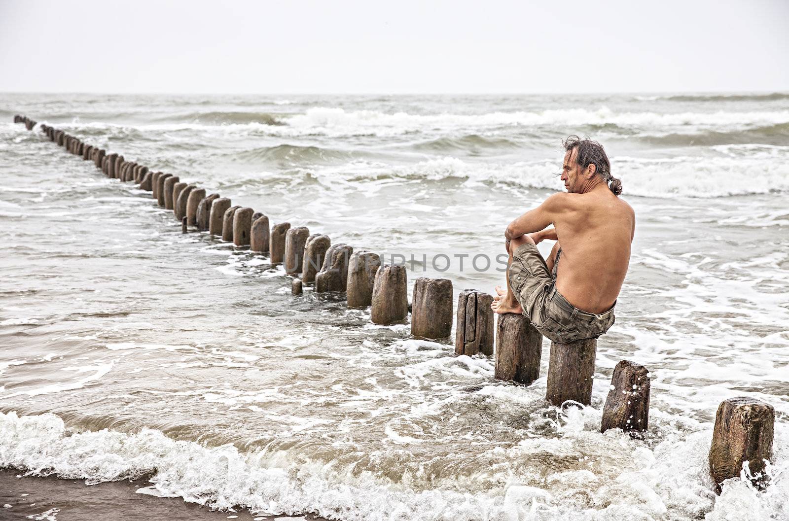 Middle-aged man sitting near the sea and looking thoughtfully into the distance