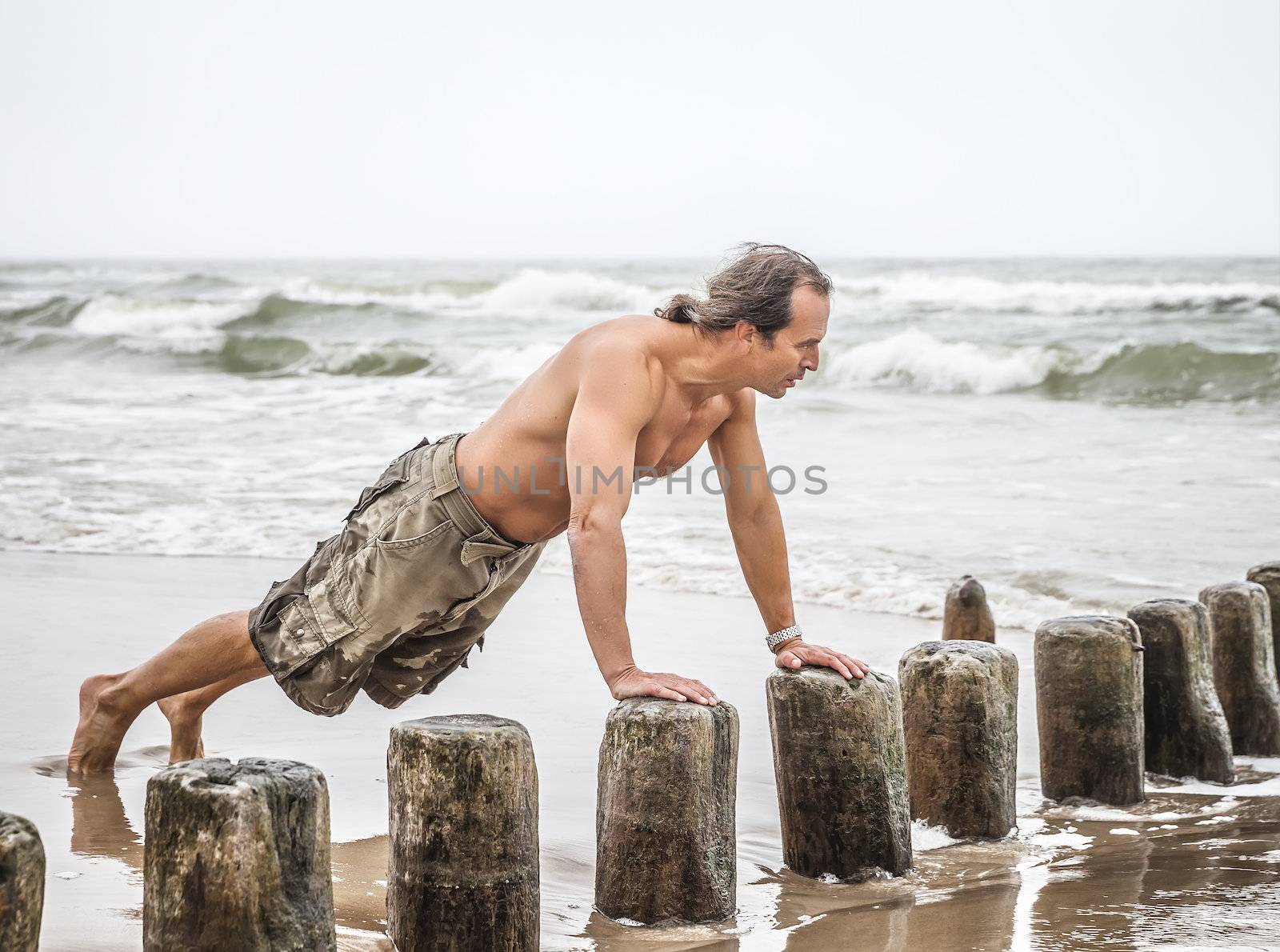 Middle-aged man doing pushups on the beach