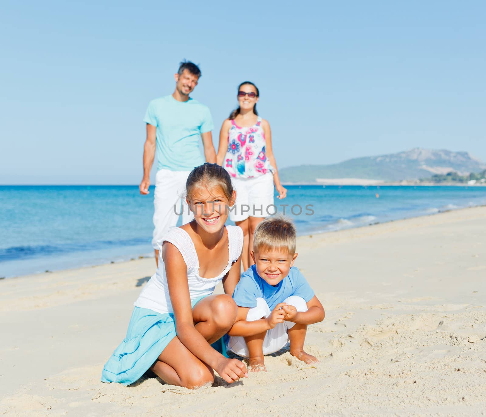 Two cute kids playing on tropical beach with their parents