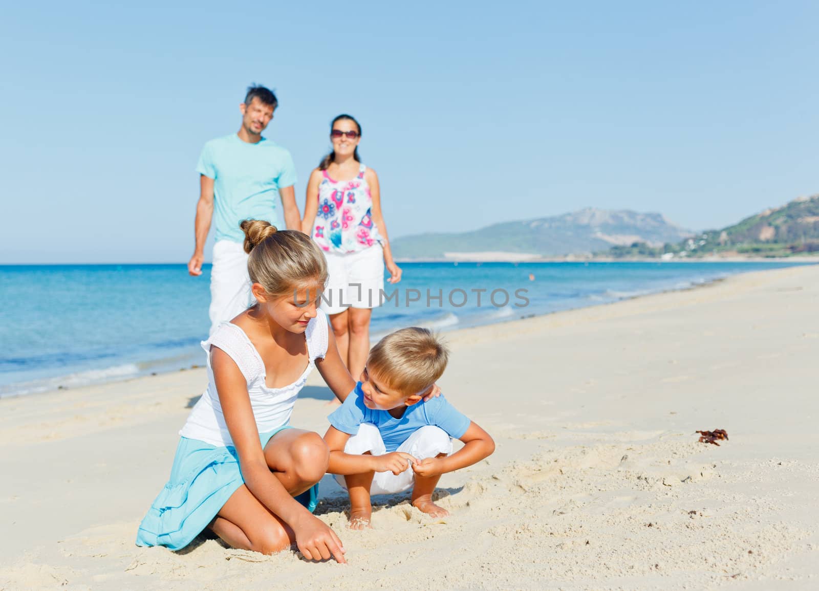 Two cute kids playing on tropical beach with their parents