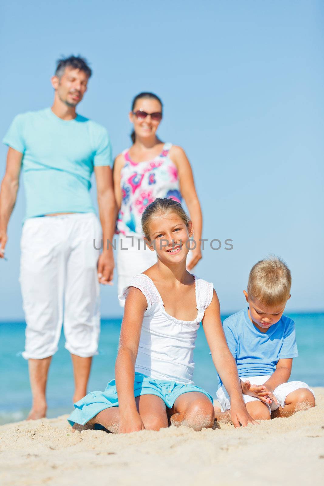 Two cute kids playing on tropical beach with their parents. Vertical view