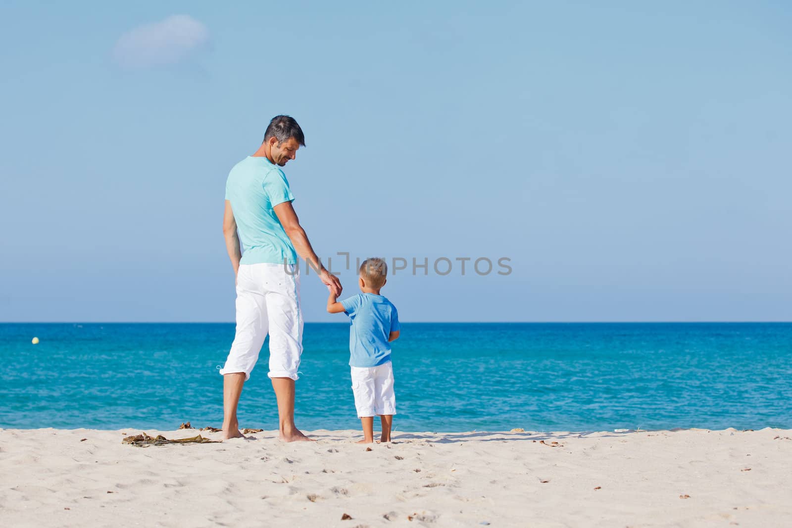 Back view of the father and son watching at the sea on tropical white sand beach