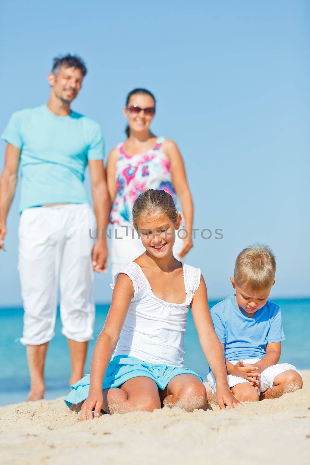 Two cute kids playing on tropical beach with their parents. Vertical view