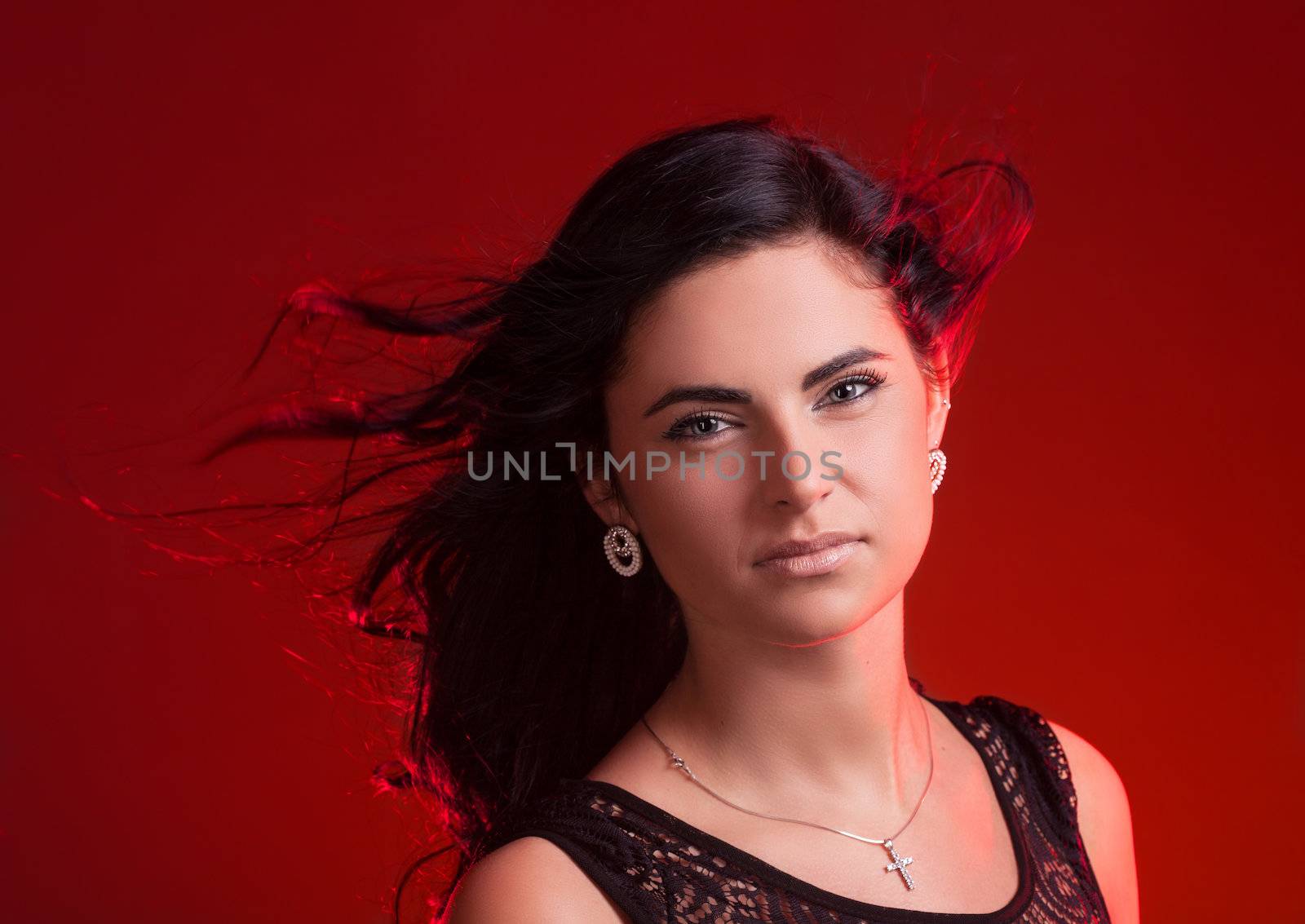 Beautiful young woman with hair blowing on wind on red background