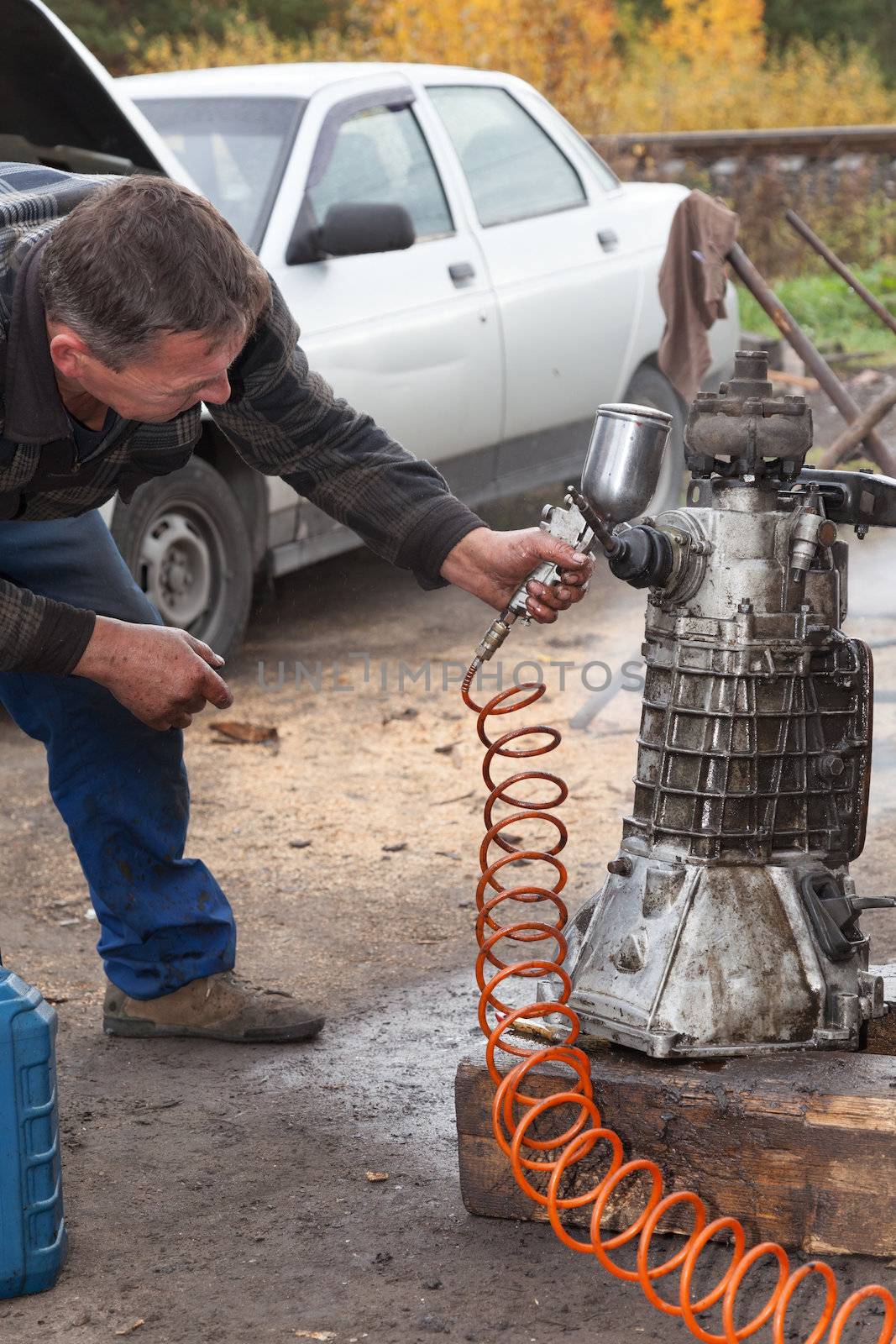 A man cleans the gearbox taken from the car for repair, using the gasoline and airbrush