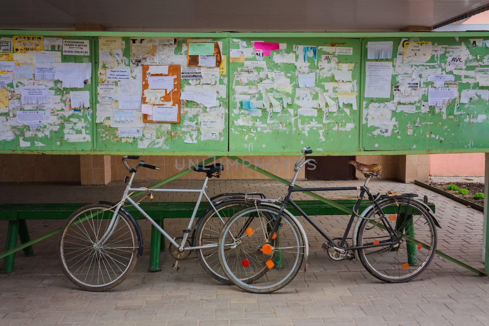 Two Old Bicycle Leaning Against A Bulletin Board On The Street. Belarus, Dobrush
