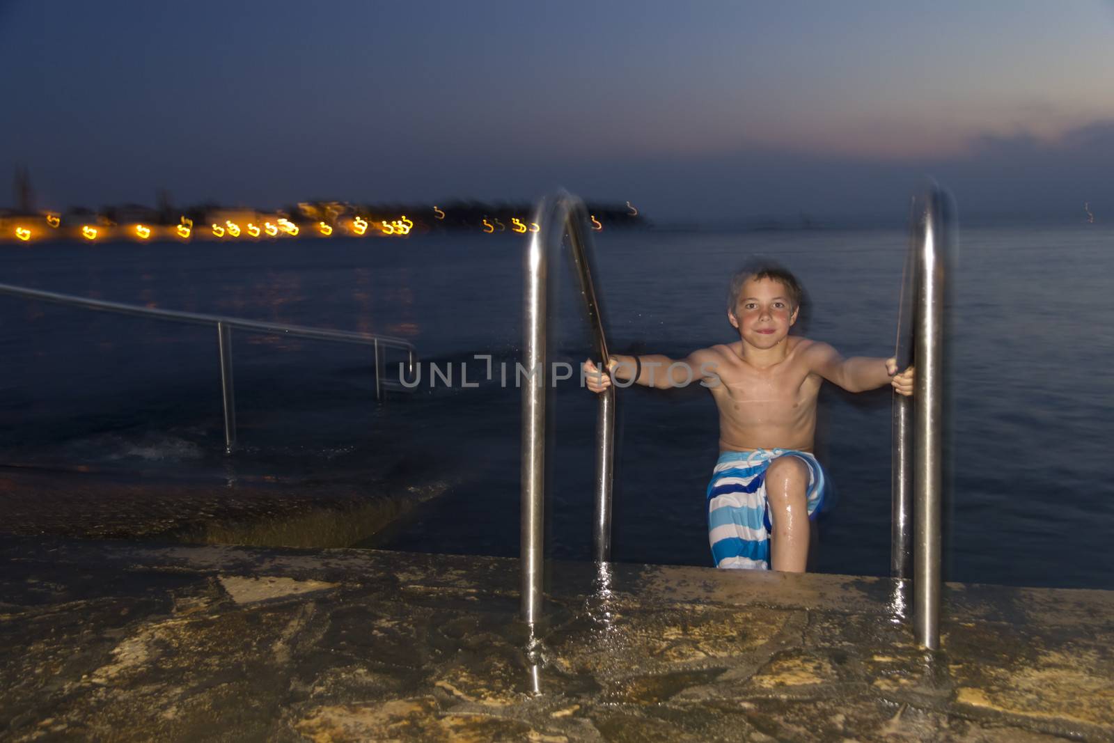 Night shot of boy getting out of the sea against the resort town by Tetyana