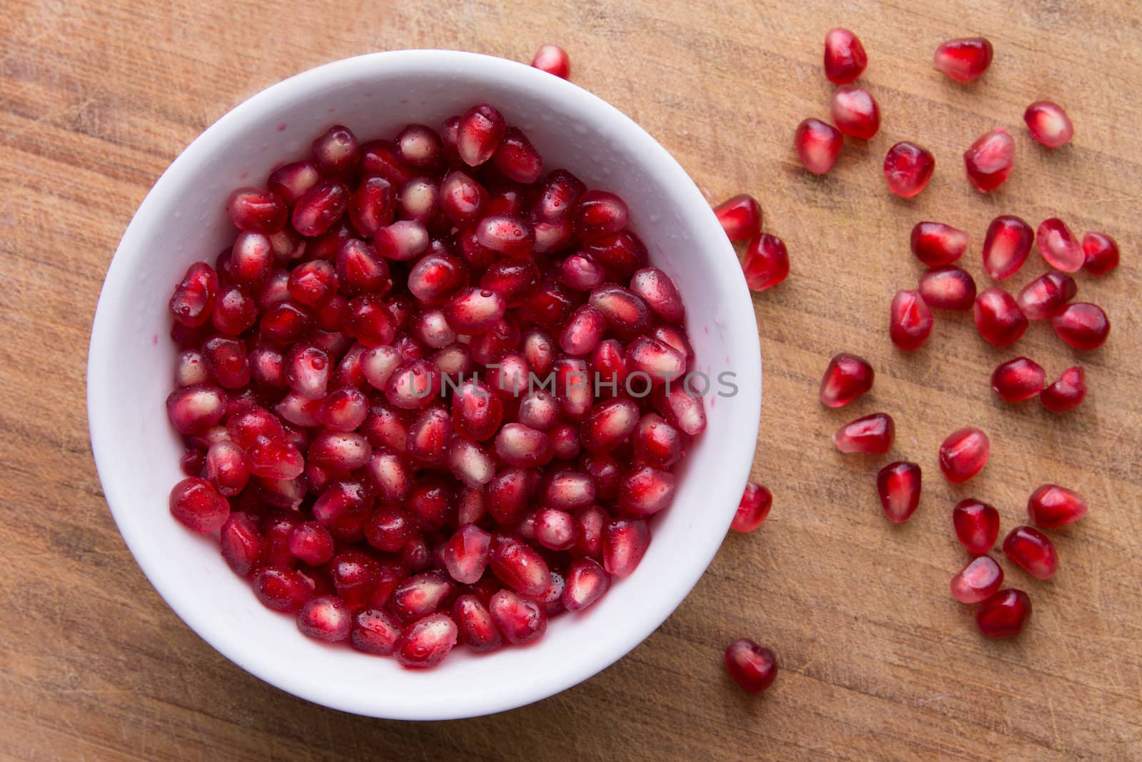 Pomegranate seeds are in a white bowl on the old cutting board