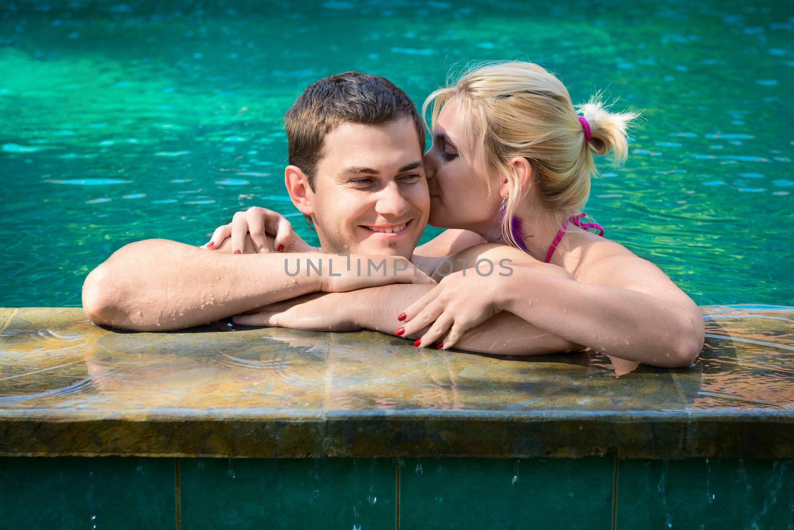 Happy smiling young couple relaxing in a swimming pool on a poolside in tropical resort
