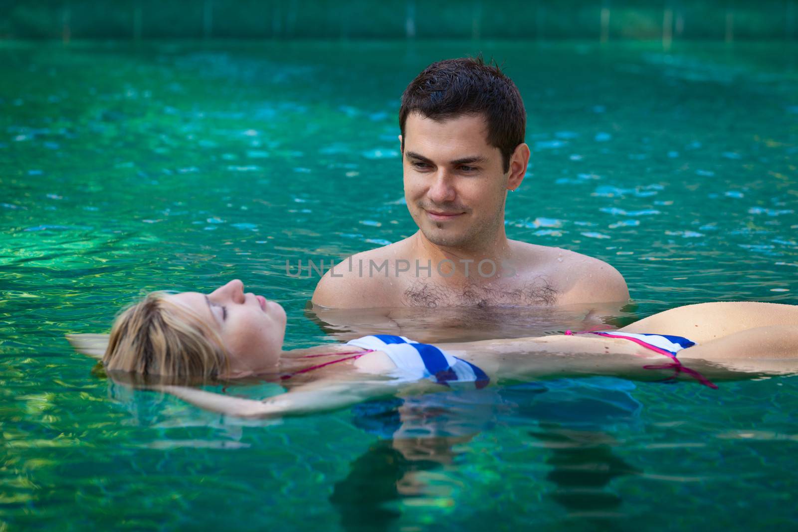 Happy smiling young couple relaxing in a swimming pool in tropical resort