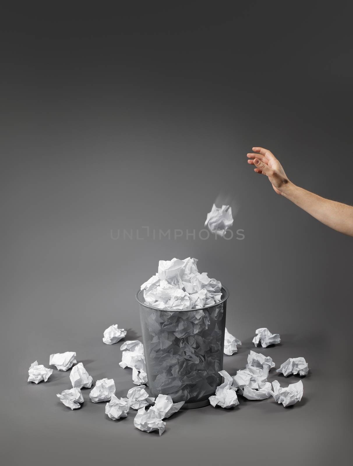 Hand throwing a crumpled paper into a waste paper basket.