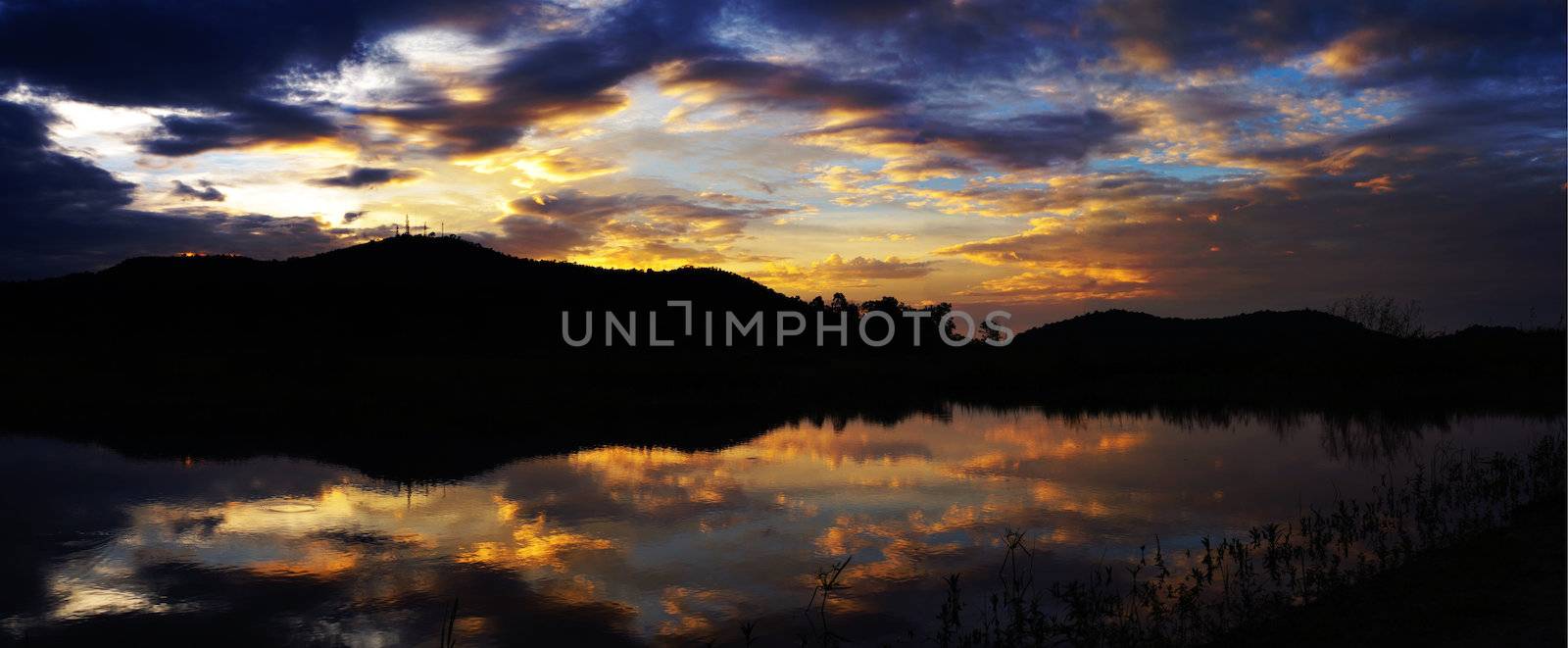 Panorama view of sunset sky with mountain silhouette and water in reservoir by pixbox77