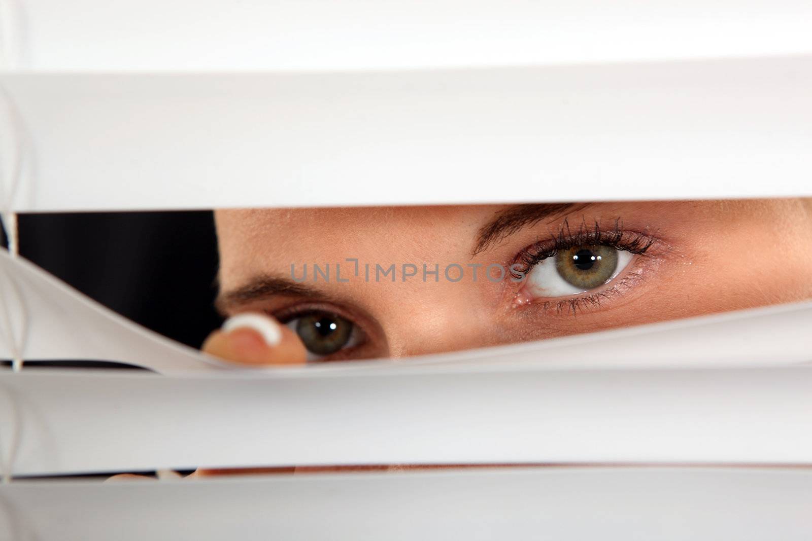 Closeup of a woman's eyes spying through blinds by phovoir