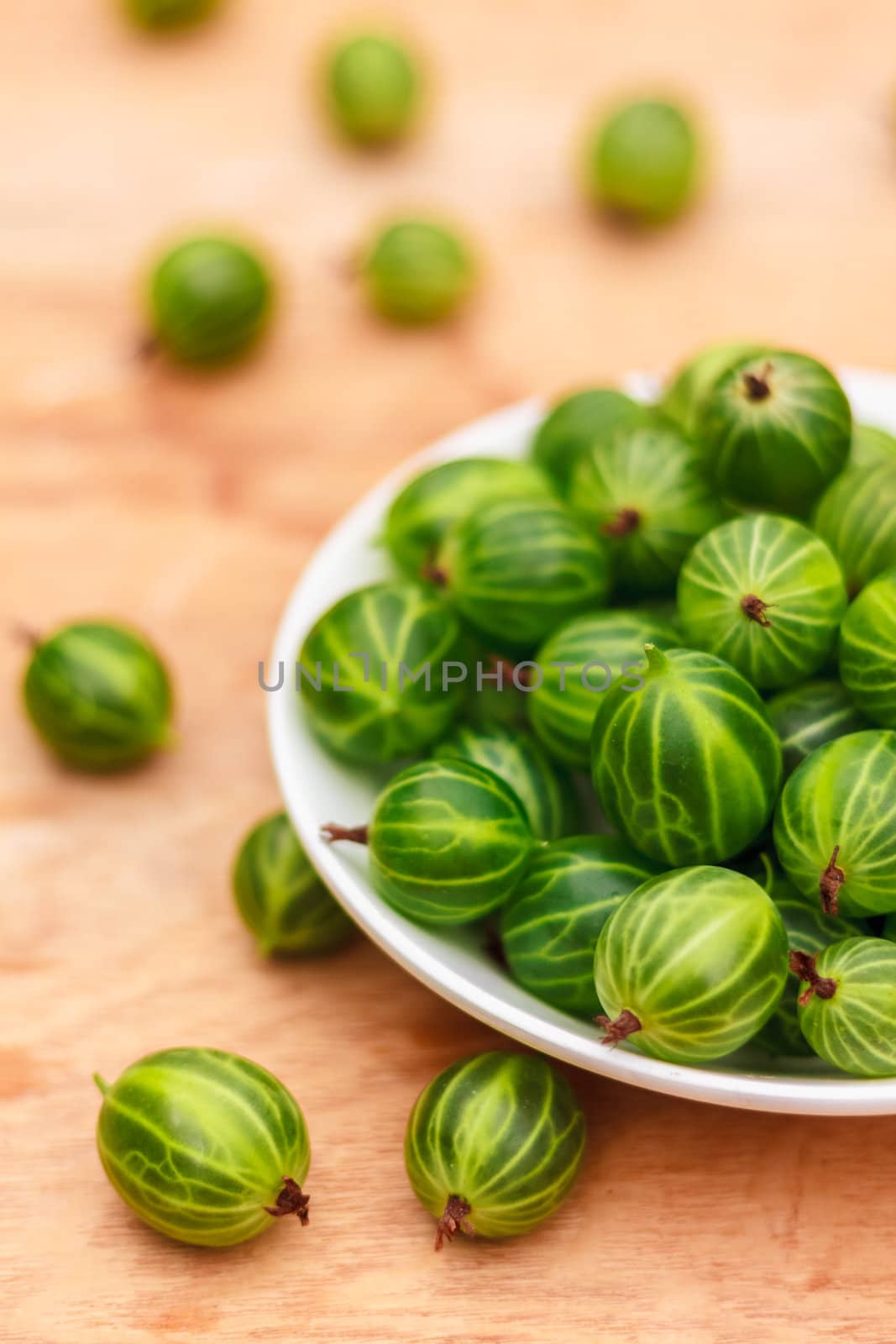 White Dish Filled With Succulent Juicy Fresh Ripe Green Gooseberries On An Old Wooden Table Top.