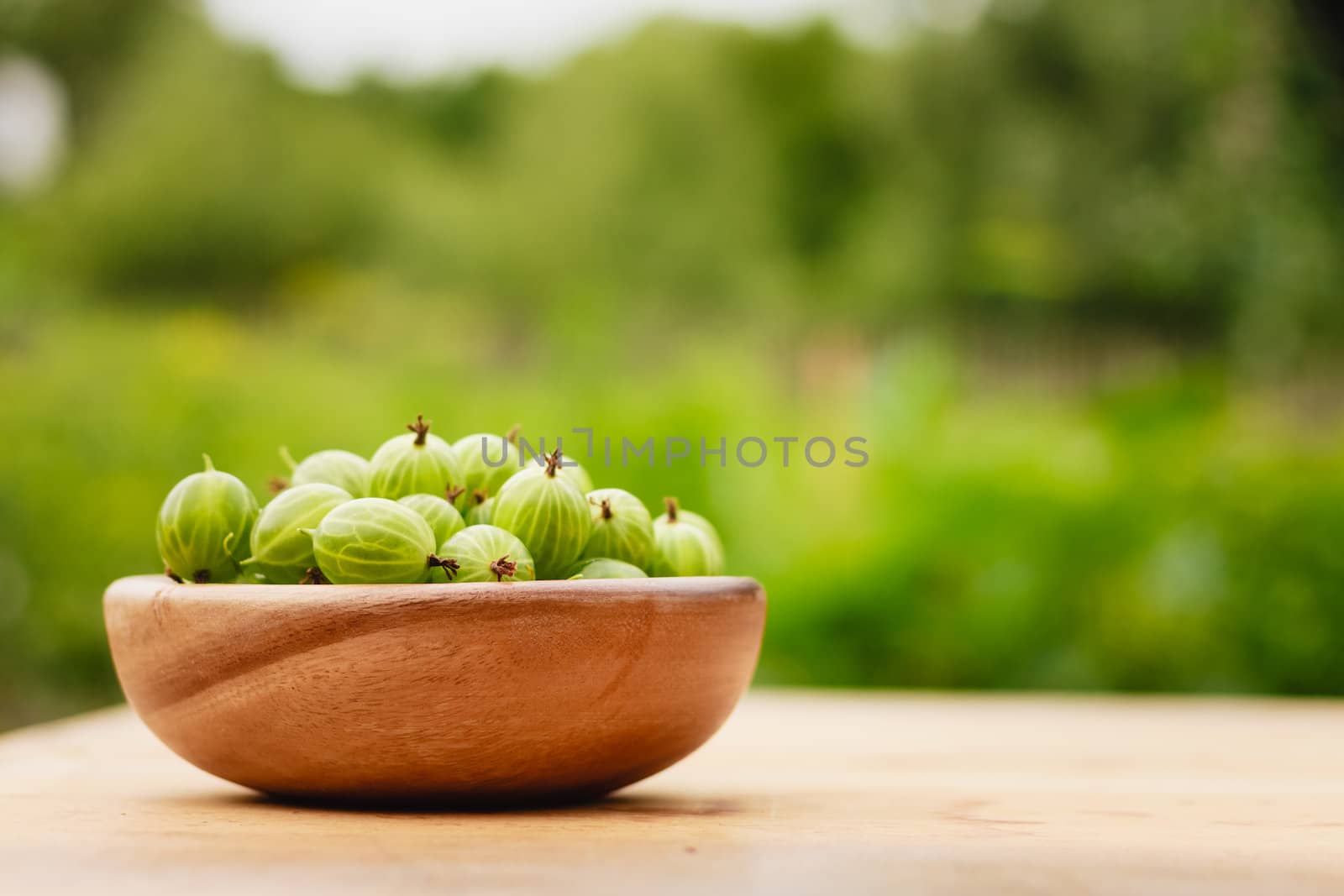 Close-Up Of Gooseberries In Vintage Wooden Bowl On Wooden Table by ryhor