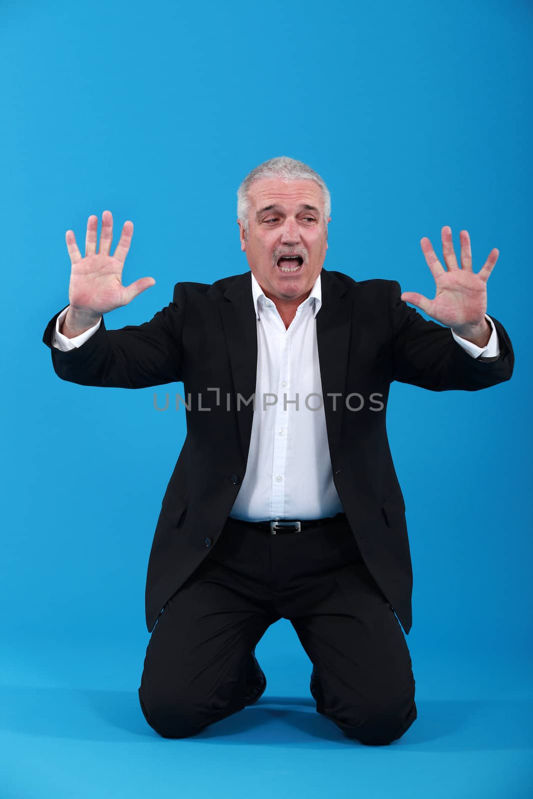 Kneeling senior man in suit screaming by phovoir