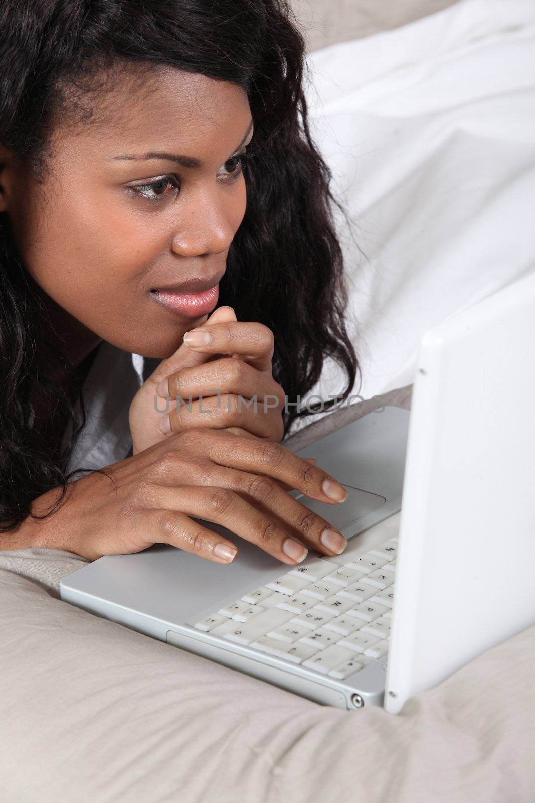 Black lady using laptop in bed by phovoir