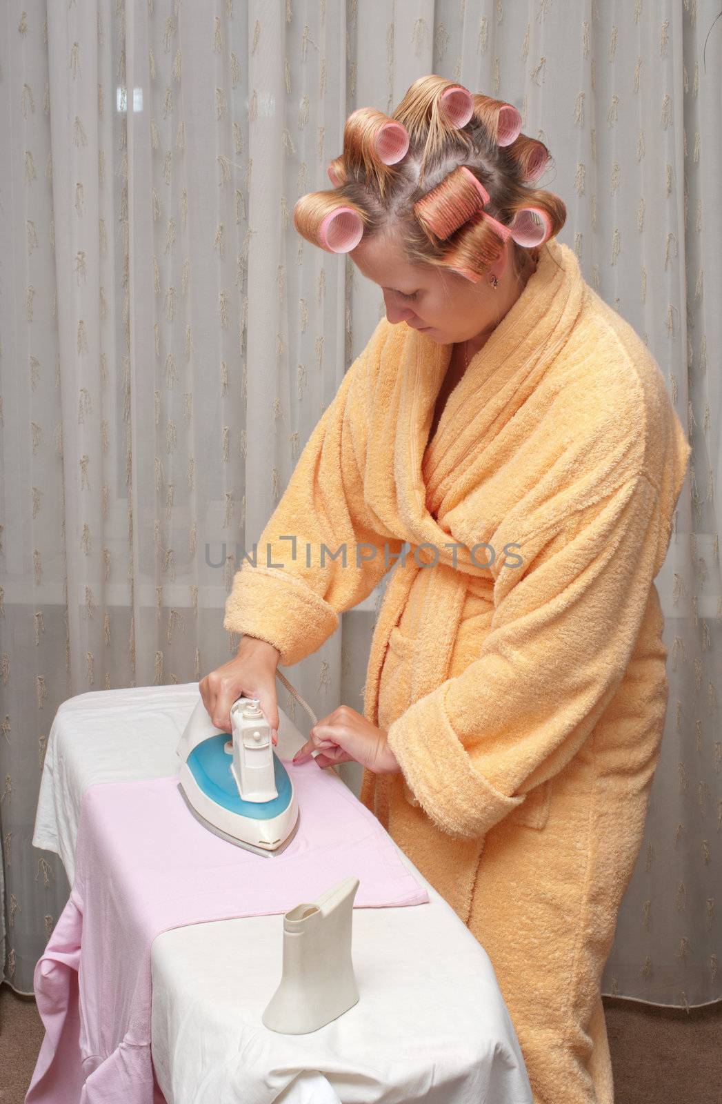 Girl with hair curlers in a dressing gown irons clothes.