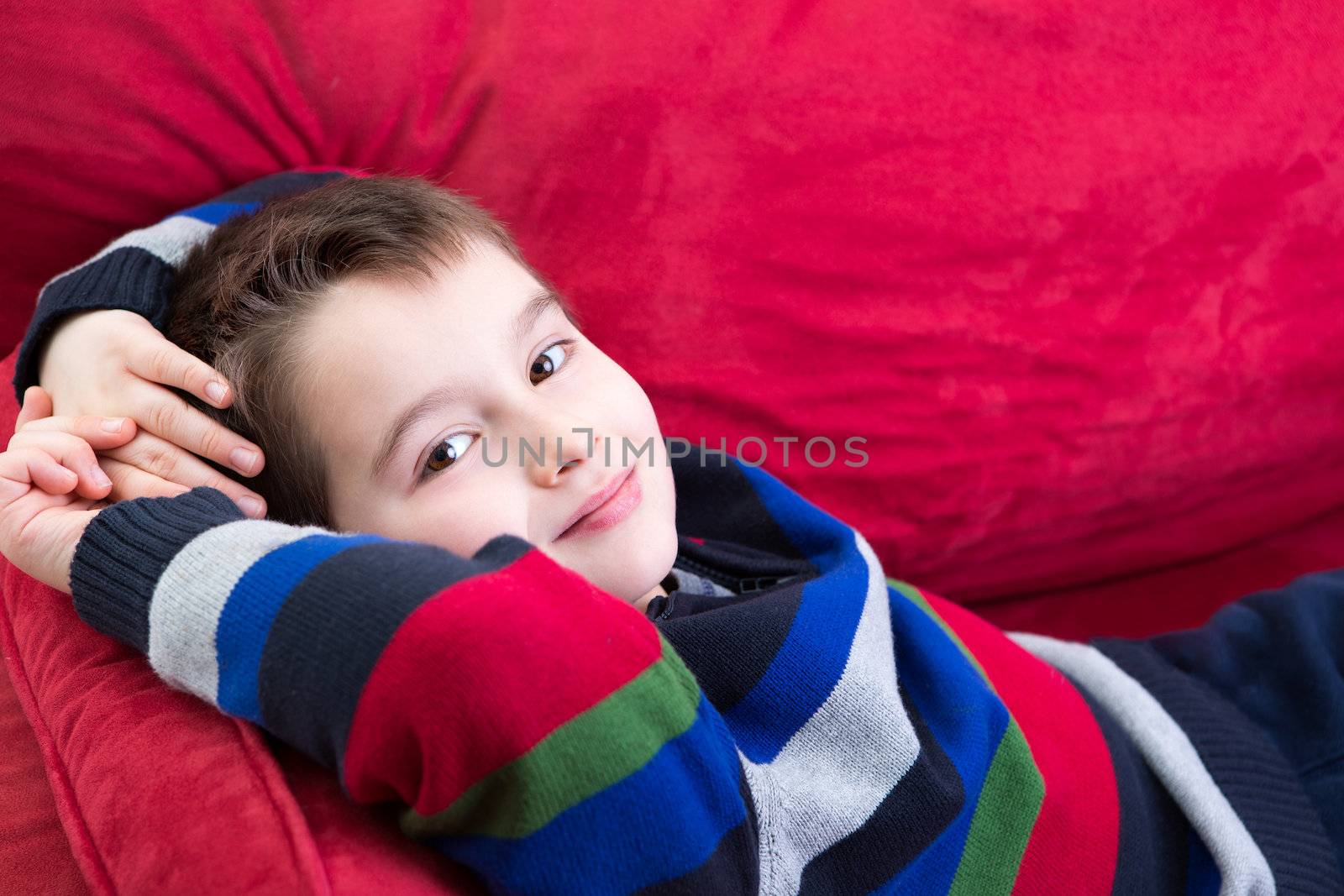 Young boy on the red couch comfortably relaxing and looking at you with confidence, perhaps he has been counseling by psychiatrist
