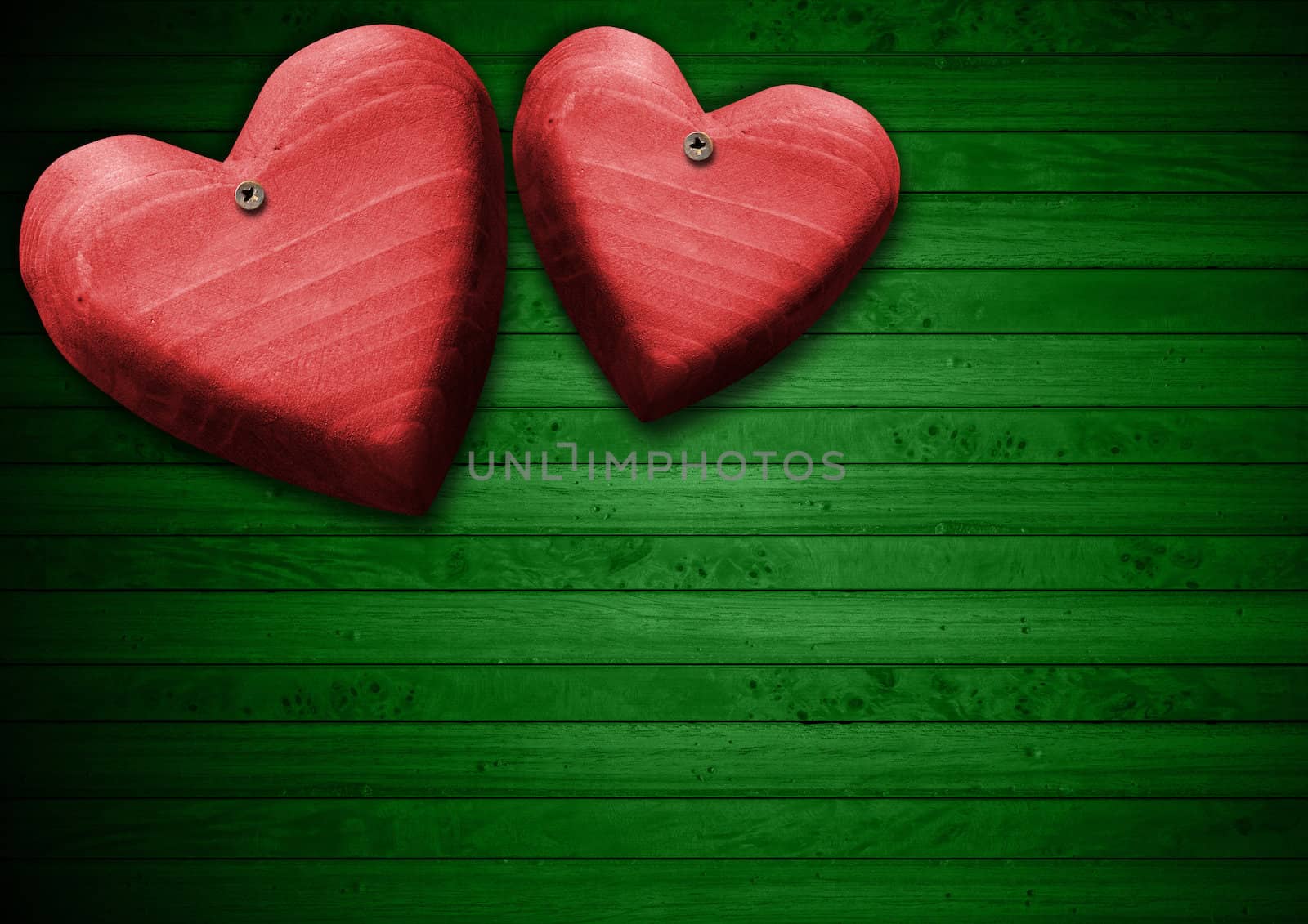 Two handmade red wooden hearts hanging on green wooden background