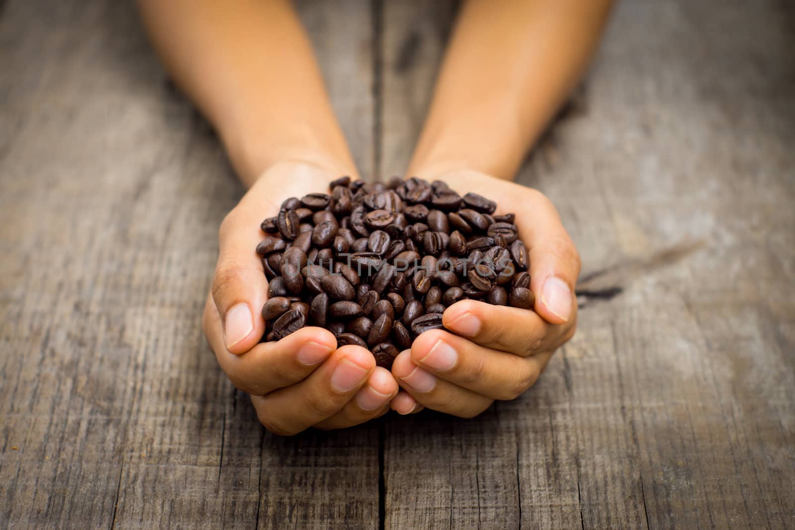 A person holding roasted coffee beans on wood background