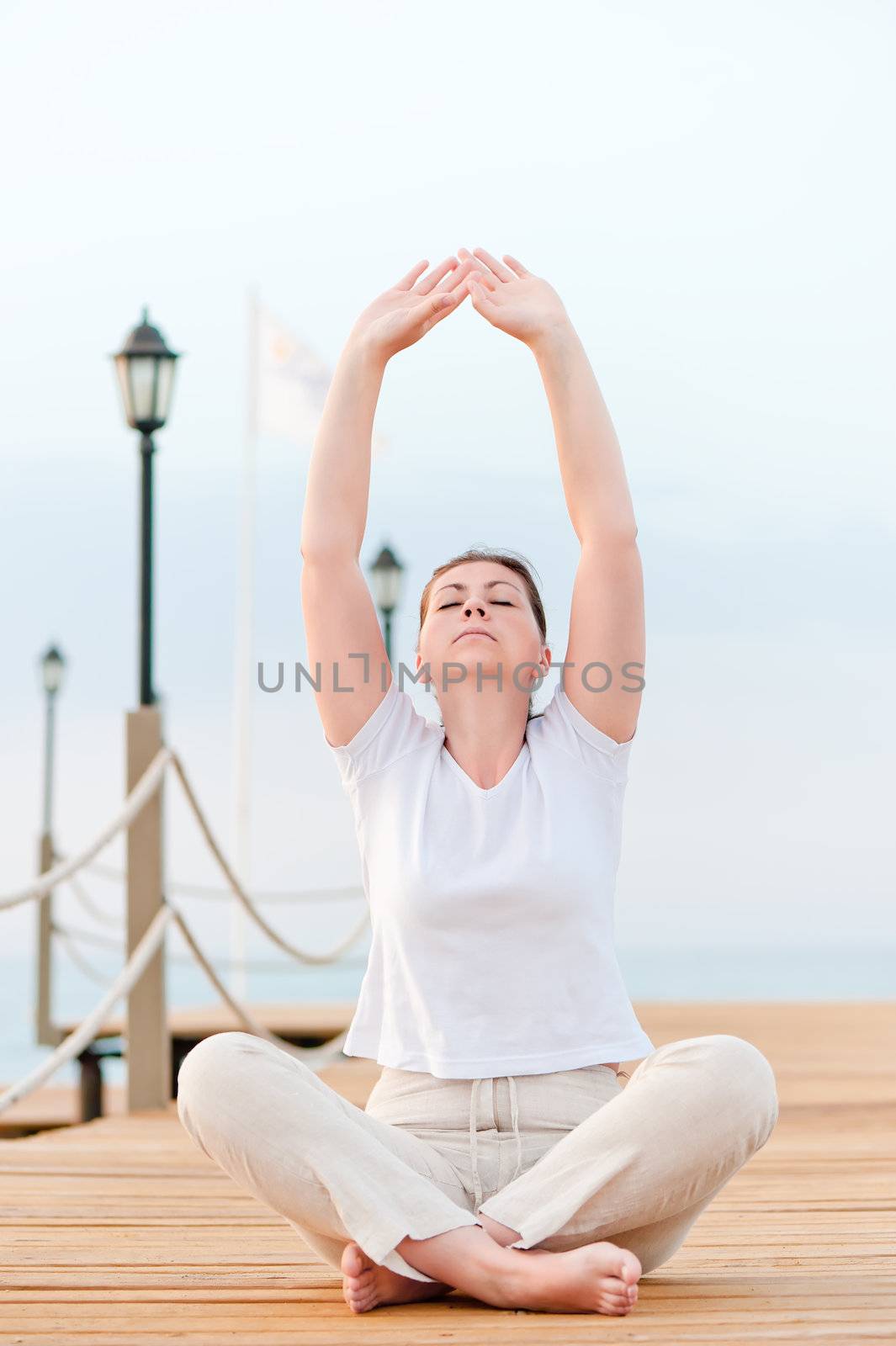 Girl stretches in the morning while sitting on a pier at the sea by kosmsos111